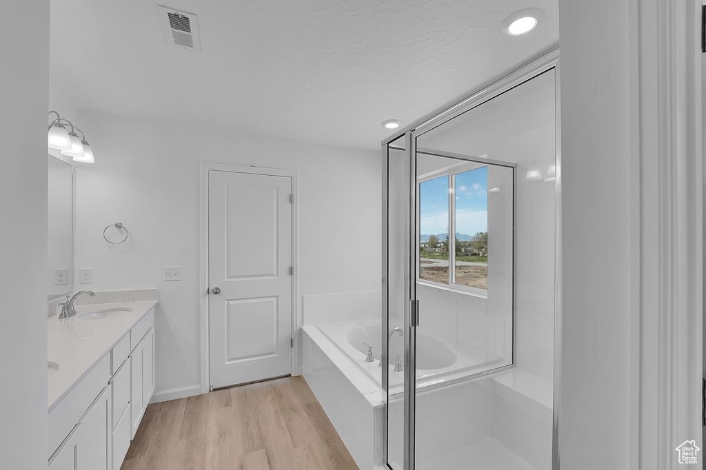 Bathroom featuring a bath, double vanity, wood finished floors, and a stall shower