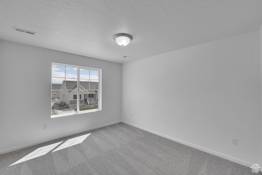 Carpeted spare room featuring baseboards and a textured ceiling