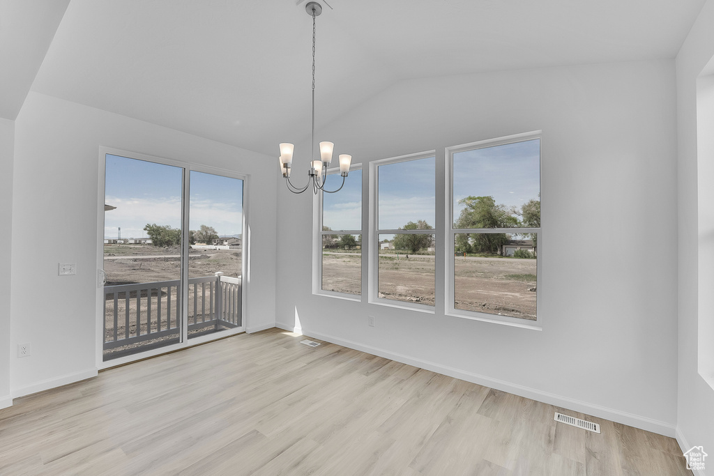 Spare room with a chandelier, wood finished floors, lofted ceiling, and baseboards
