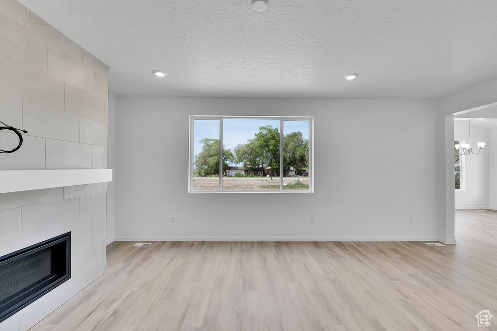 Unfurnished living room with light wood finished floors, a chandelier, a tile fireplace, baseboards, and recessed lighting