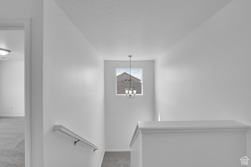 Stairs featuring carpet flooring, a textured ceiling, baseboards, and a chandelier