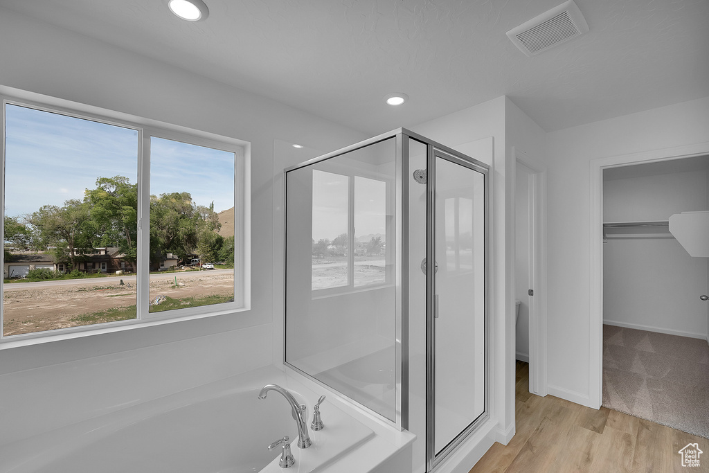 Bathroom featuring a stall shower, a garden tub, a spacious closet, recessed lighting, and wood finished floors