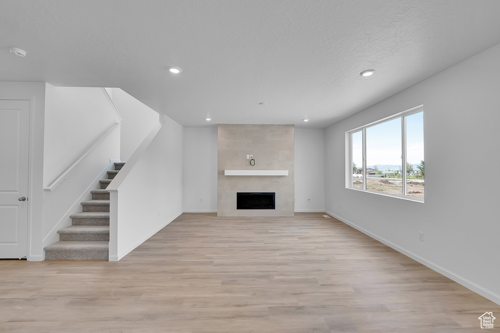 Unfurnished living room featuring recessed lighting, baseboards, stairway, light wood-style flooring, and a large fireplace