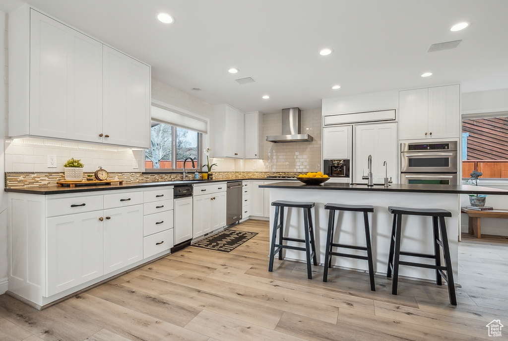 Kitchen featuring dark countertops, wall chimney exhaust hood, a breakfast bar area, and a sink