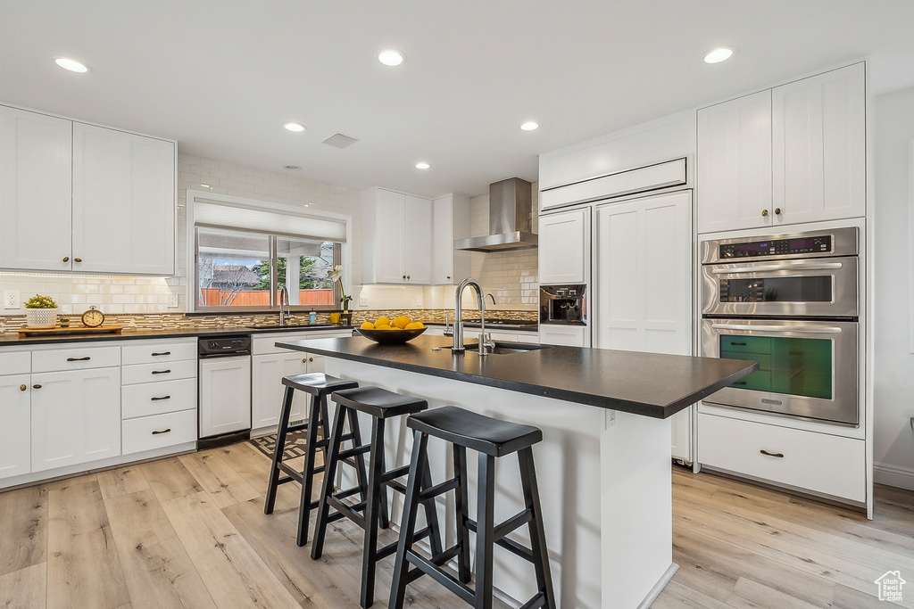 Kitchen featuring dark countertops, double oven, light wood-style floors, and wall chimney range hood