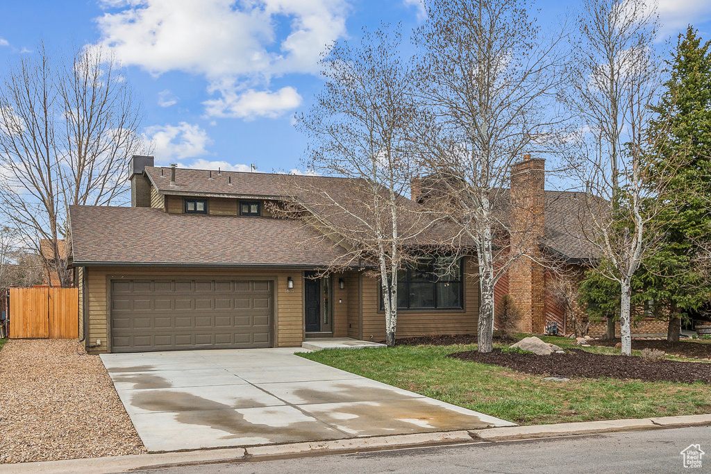 View of front facade featuring a chimney, concrete driveway, an attached garage, fence, and roof with shingles