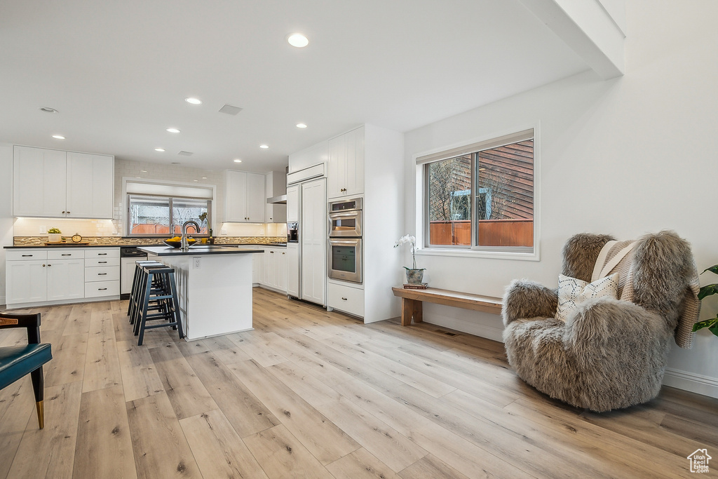 Kitchen with light wood finished floors, dark countertops, a sink, and white cabinetry