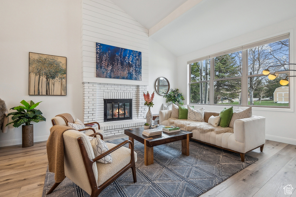 Living area with high vaulted ceiling, baseboards, a brick fireplace, and light wood-style flooring