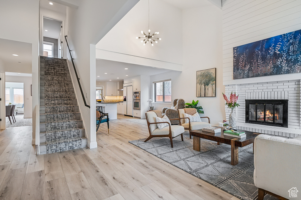 Living area featuring light wood-type flooring, a brick fireplace, a high ceiling, and stairway