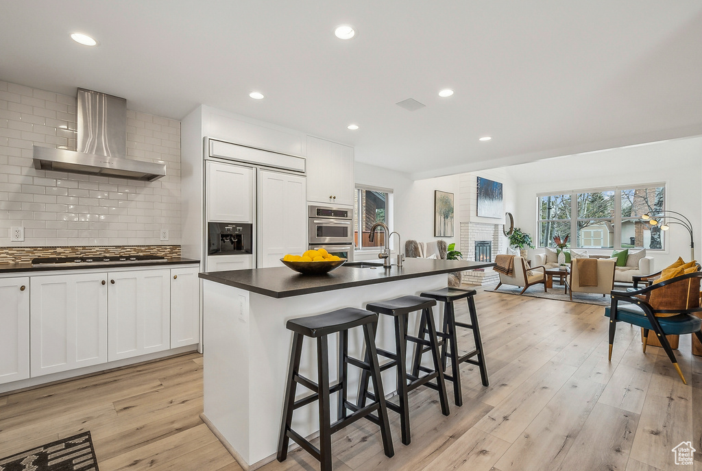Kitchen featuring wall chimney exhaust hood, dark countertops, a sink, and appliances with stainless steel finishes