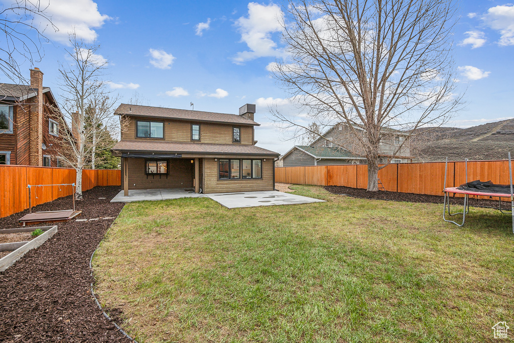 Rear view of property with a patio area, a trampoline, a chimney, a fenced backyard, and a yard