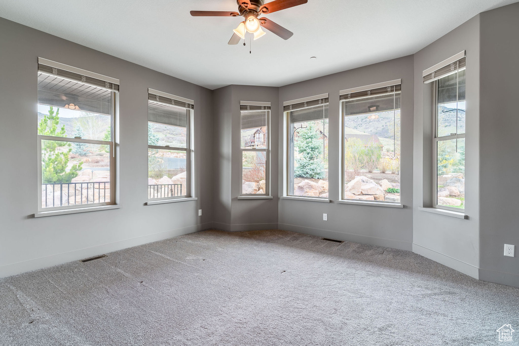 Carpeted empty room featuring plenty of natural light, visible vents, and a ceiling fan