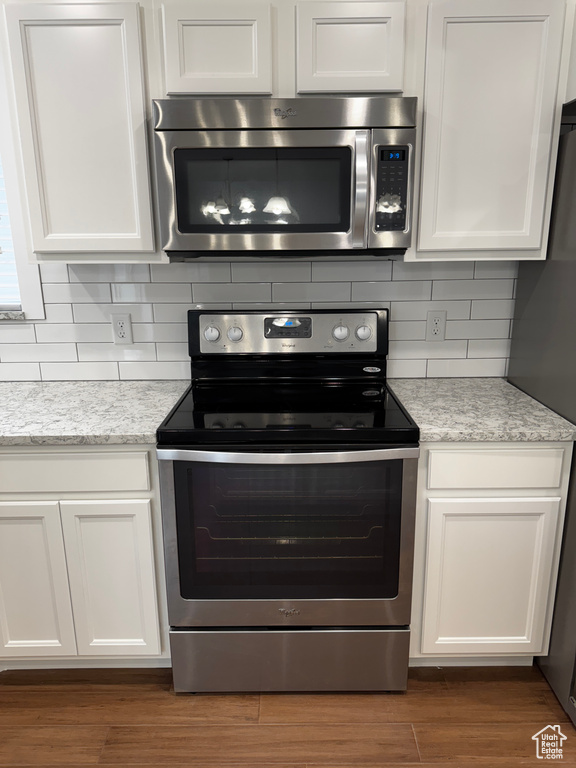 Kitchen with backsplash, appliances with stainless steel finishes, and white cabinets