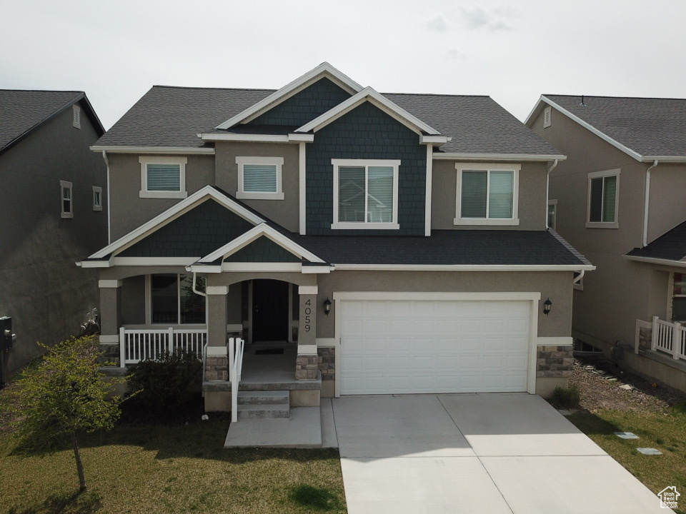 Craftsman-style home featuring stone siding, concrete driveway, covered porch, an attached garage, and a front yard