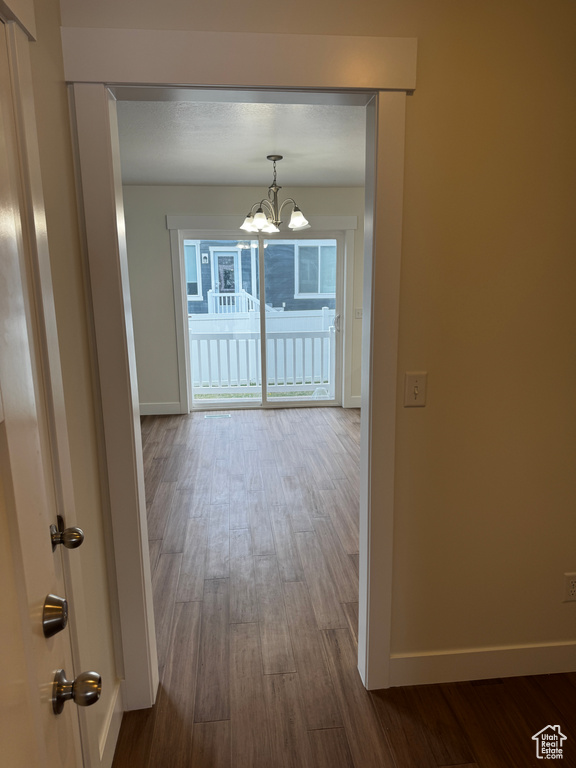 Corridor featuring baseboards, an inviting chandelier, and dark wood finished floors