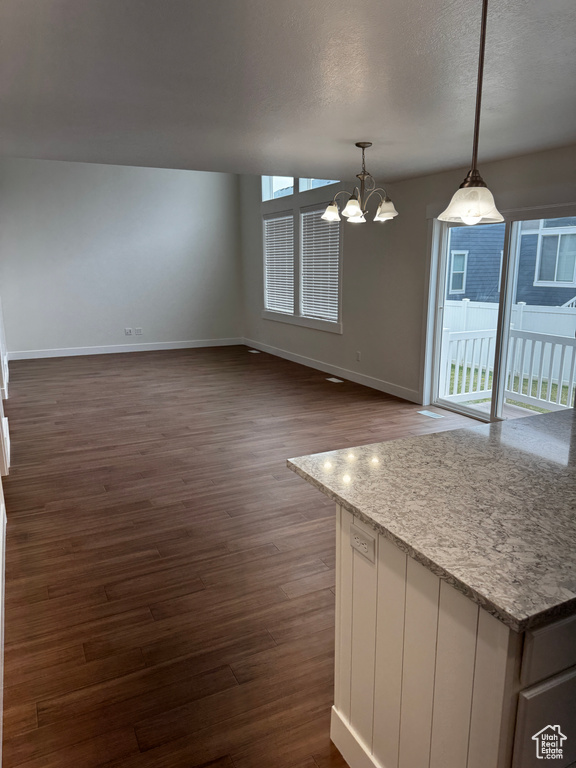 Unfurnished dining area featuring dark wood finished floors, a textured ceiling, baseboards, and a notable chandelier