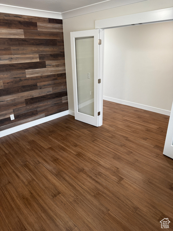 Unfurnished room with baseboards, dark wood-type flooring, and wooden walls