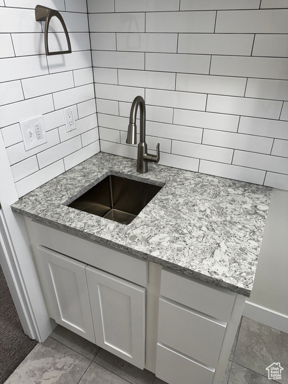 Kitchen featuring light stone counters, a sink, decorative backsplash, baseboards, and white cabinetry