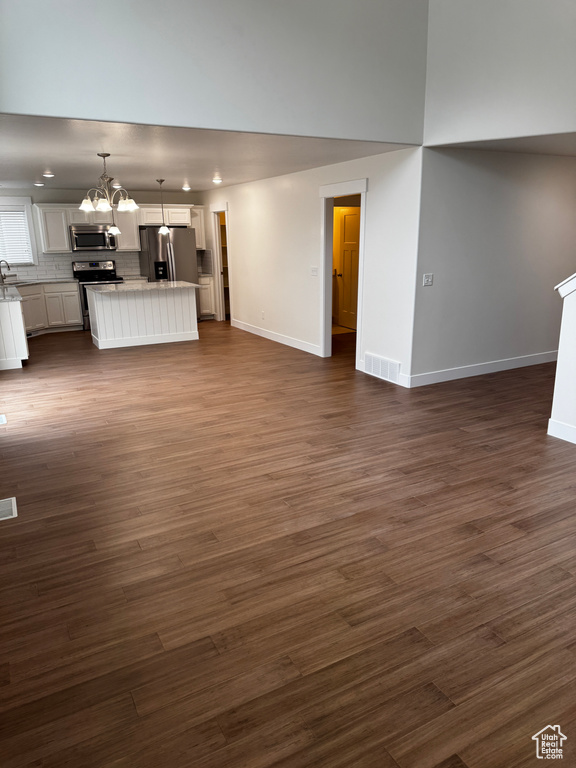 Unfurnished living room featuring visible vents, dark wood-type flooring, baseboards, and a notable chandelier