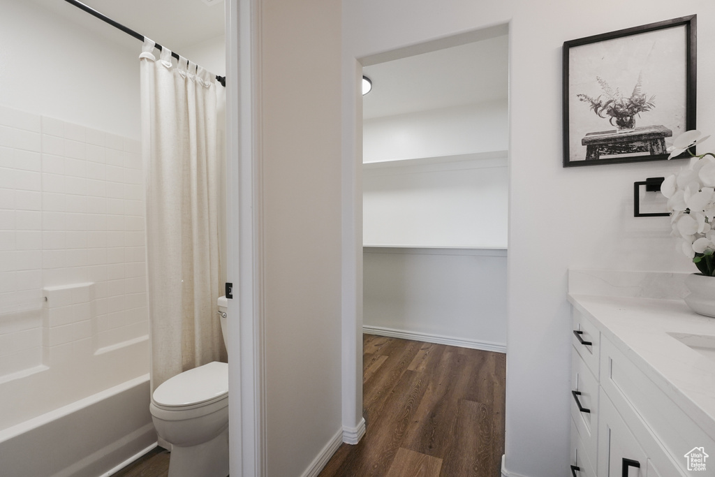Full bathroom with wood finished floors, toilet, vanity, shower / bath combo with shower curtain, and baseboards