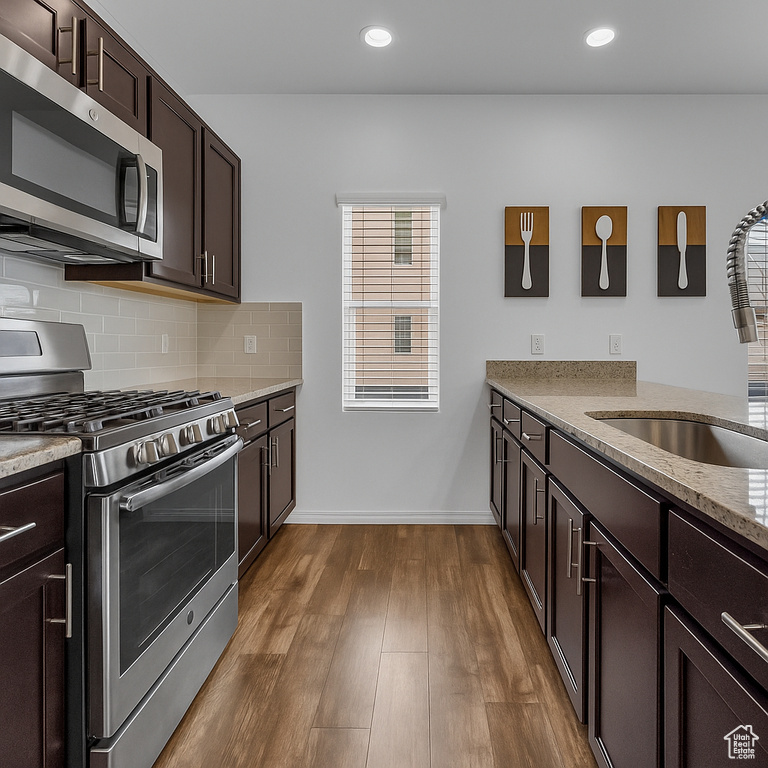 Kitchen featuring stainless steel appliances, a sink, light stone countertops, dark brown cabinets, and tasteful backsplash