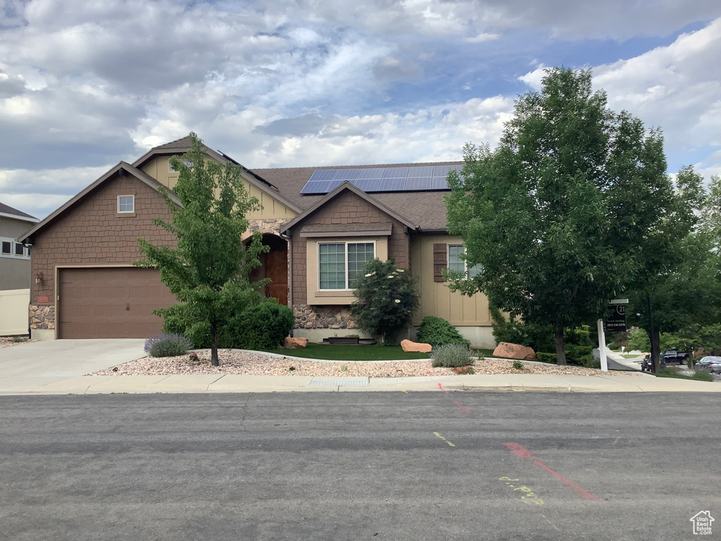 View of front of home with solar panels, driveway, a garage, and stone siding