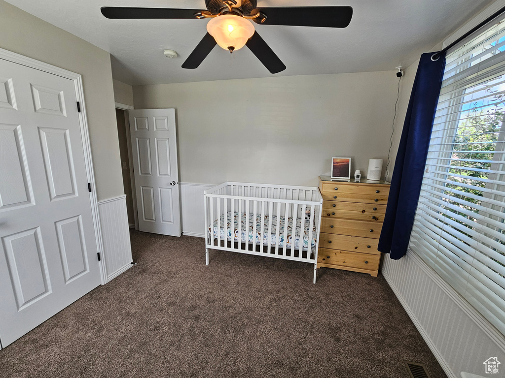 Bedroom with wainscoting, carpet floors, a ceiling fan, and a crib