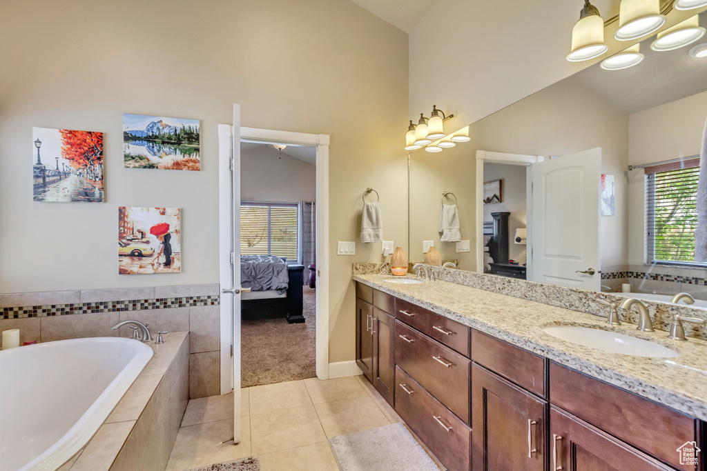 Ensuite bathroom featuring double vanity, lofted ceiling, tile patterned floors, and a sink