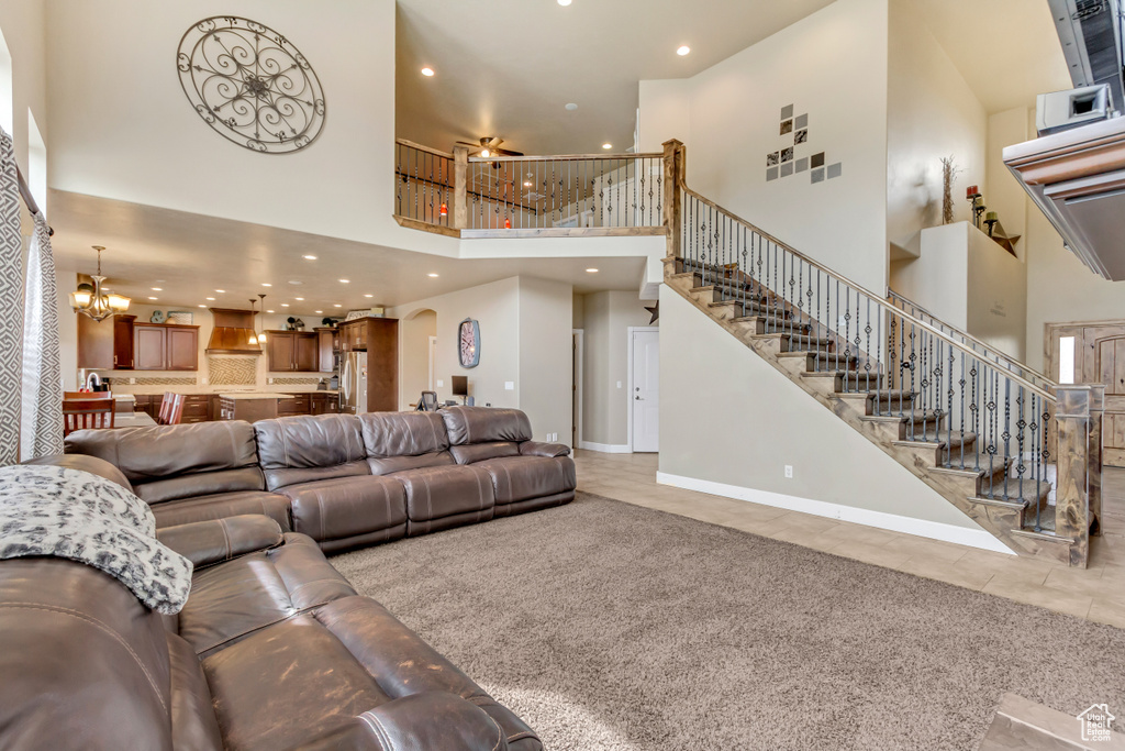 Tiled living area with stairs, ceiling fan with notable chandelier, a towering ceiling, baseboards, and recessed lighting