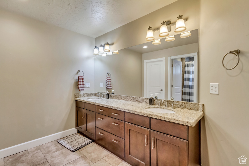 Full bath with double vanity, tile patterned flooring, baseboards, and a sink