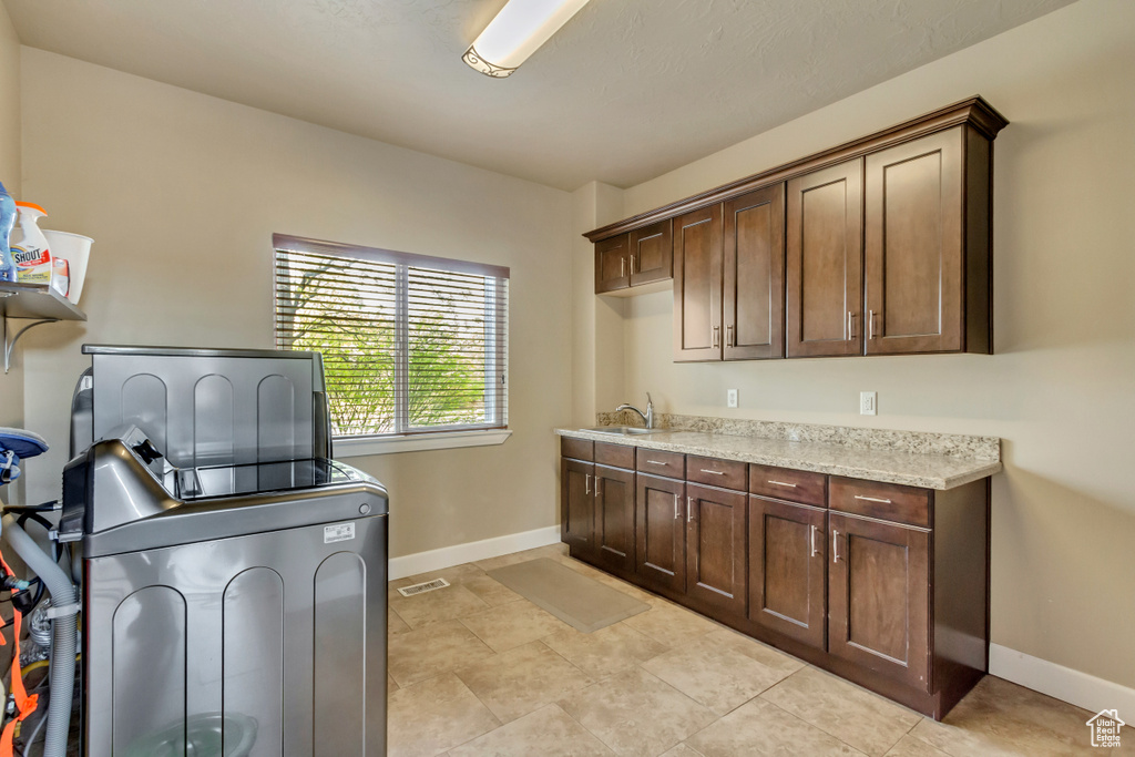 Clothes washing area with a sink, washer / dryer, cabinet space, baseboards, and visible vents