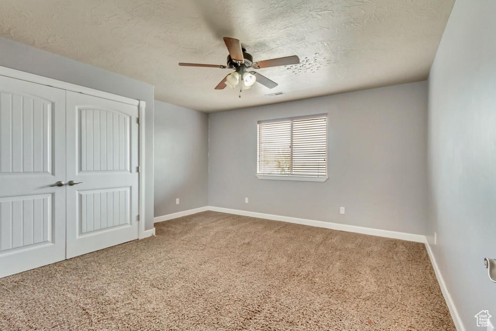 Unfurnished bedroom with a ceiling fan, a textured ceiling, a closet, carpet, and baseboards