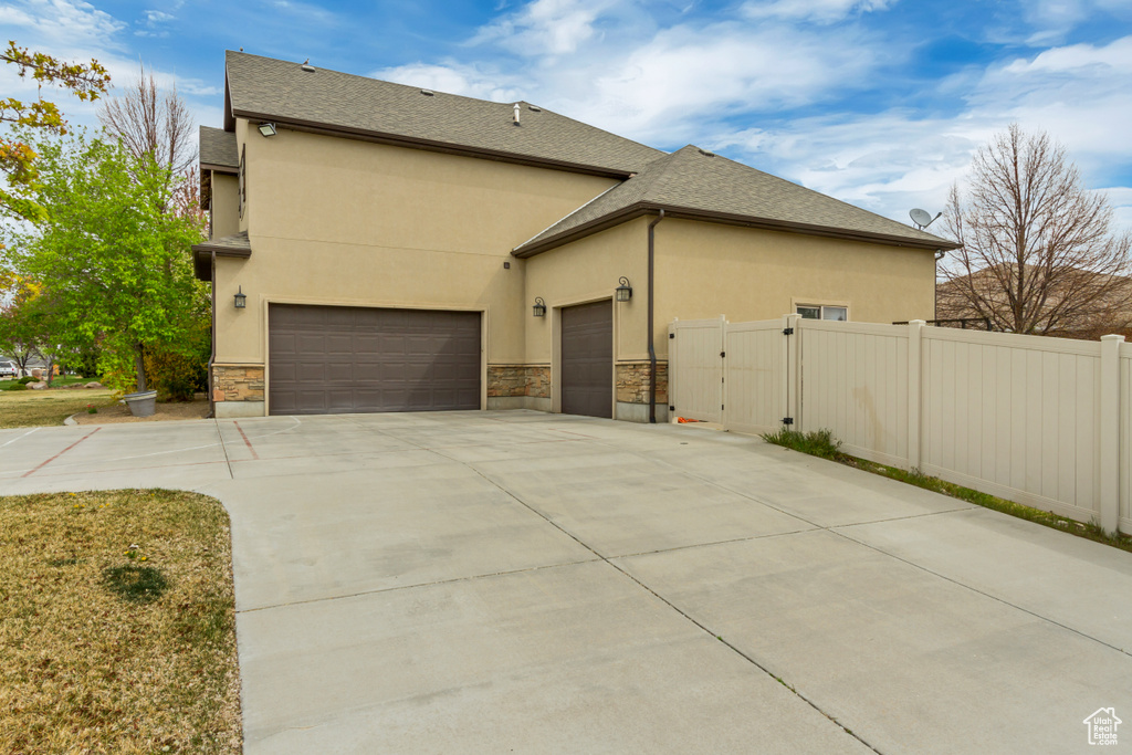 View of property exterior with a gate, an attached garage, stone siding, and concrete driveway