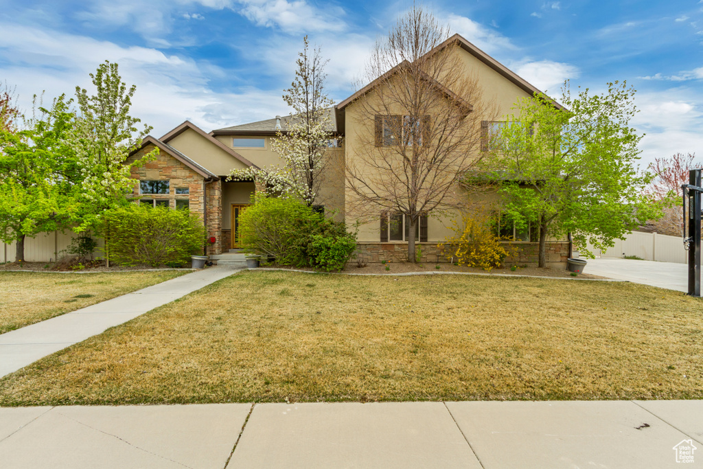 View of front of house featuring stone siding, a front lawn, fence, and stucco siding