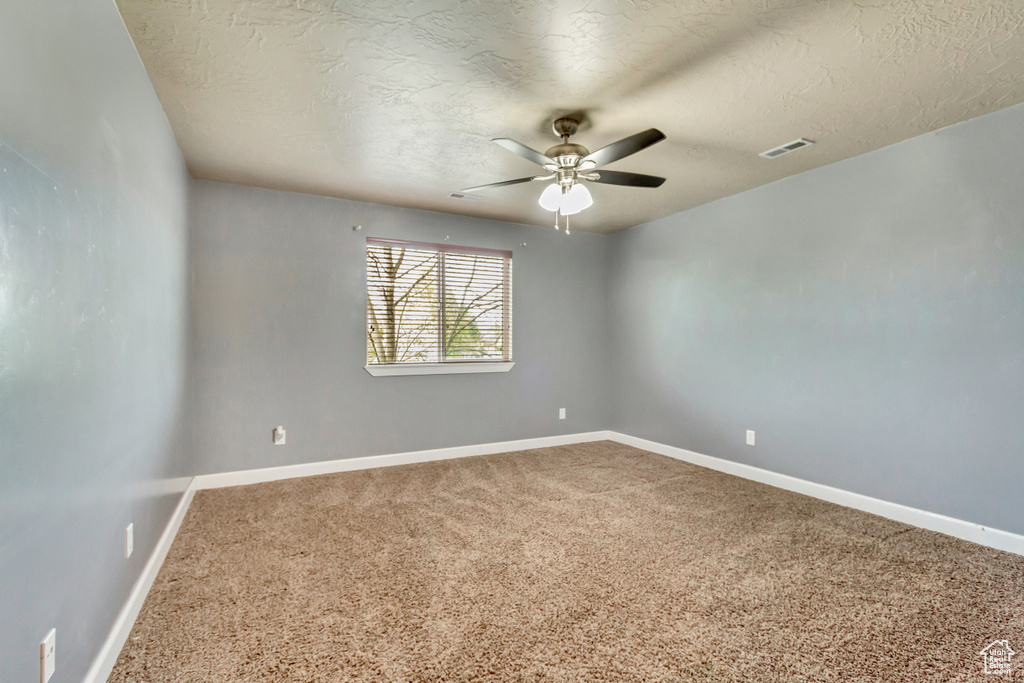 Unfurnished room featuring a ceiling fan, a textured ceiling, carpet, baseboards, and visible vents