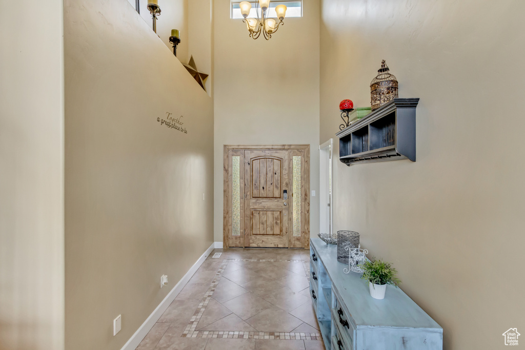 Entryway featuring baseboards, a chandelier, a towering ceiling, and light tile patterned floors