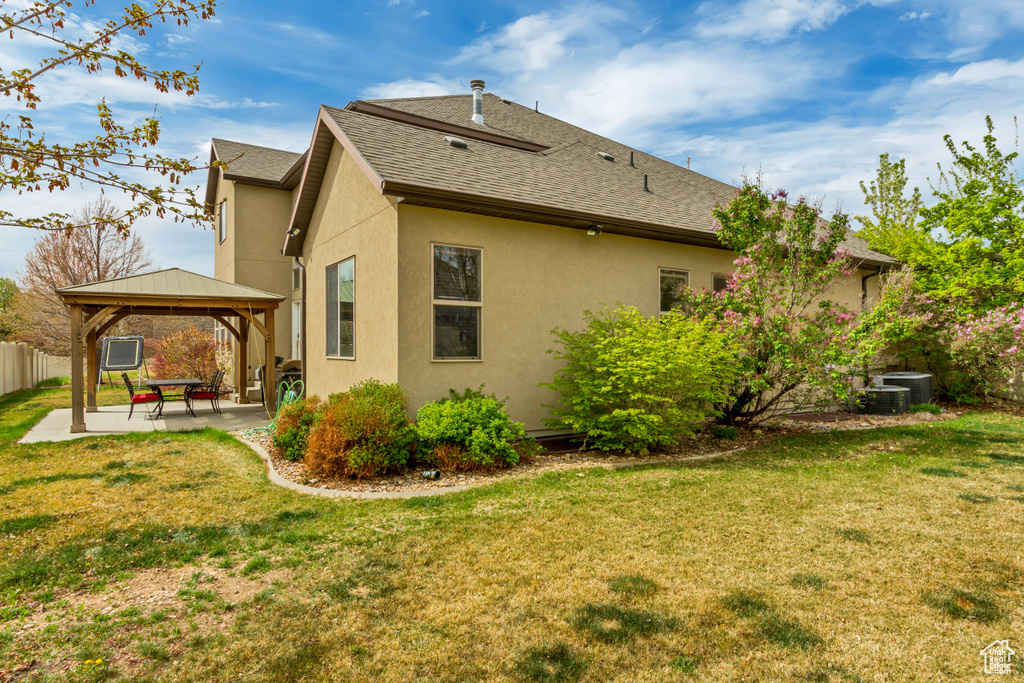 Rear view of property featuring a gazebo, a patio area, a shingled roof, a yard, and stucco siding