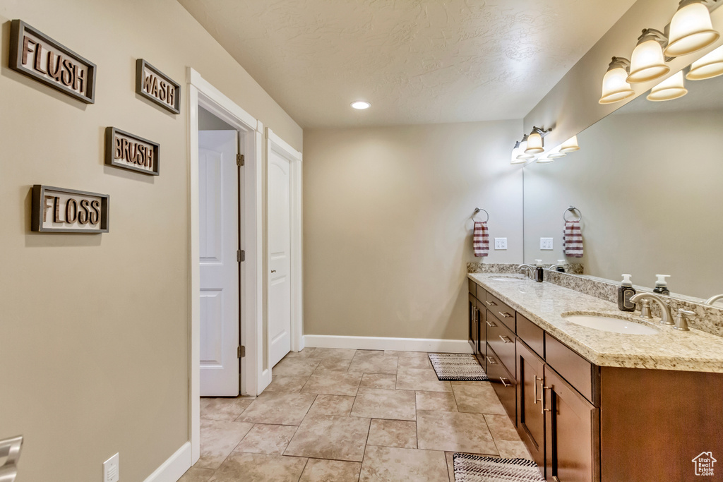 Full bath featuring double vanity, a textured ceiling, baseboards, and a sink