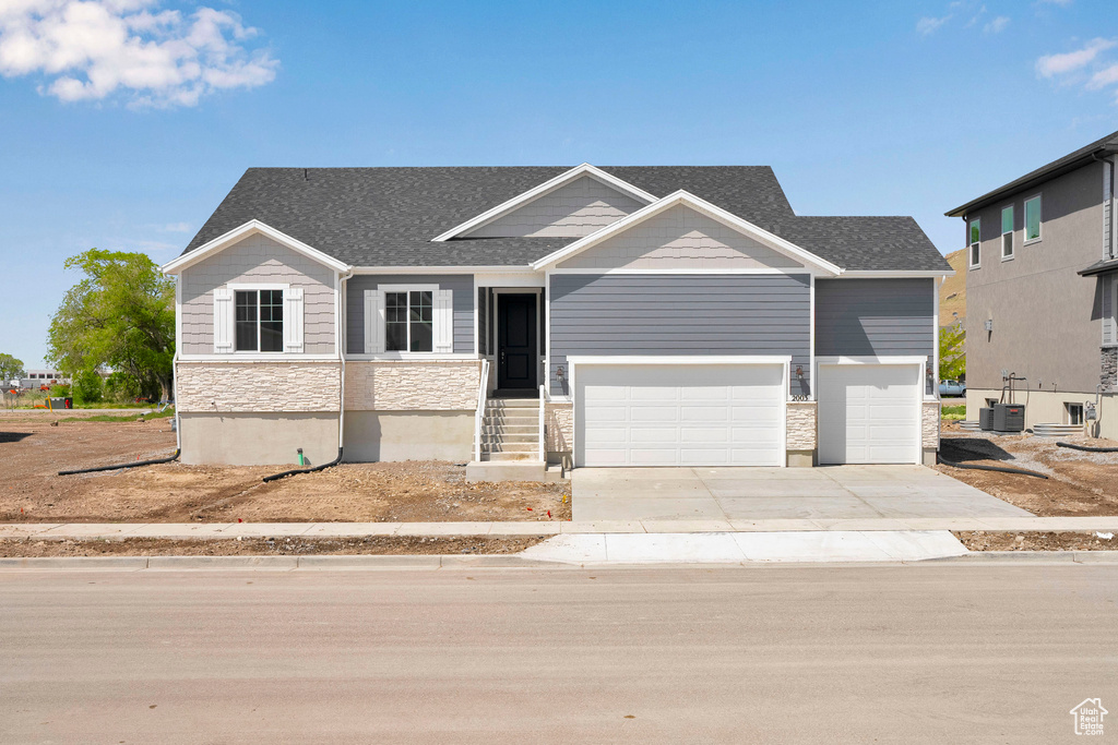 Craftsman house with stone siding, concrete driveway, an attached garage, a shingled roof, and central AC unit