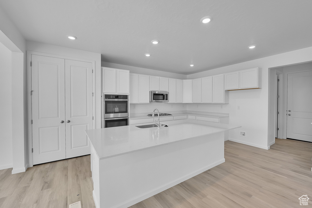 Kitchen with stainless steel appliances, white cabinetry, baseboards, light wood-type flooring, and recessed lighting