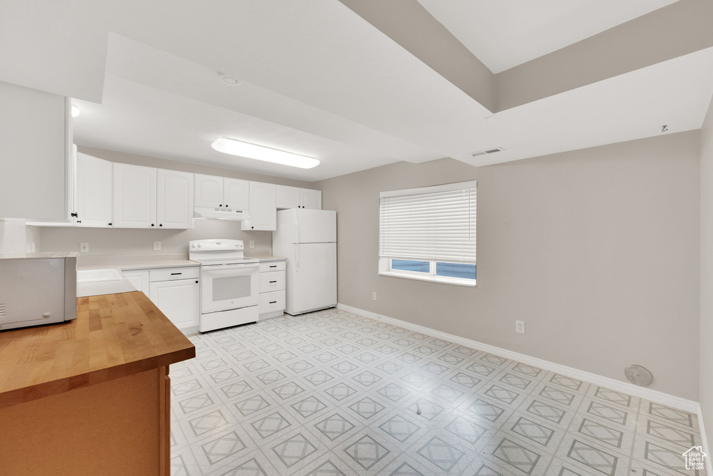 Kitchen featuring white appliances, butcher block countertops, light flooring, baseboards, and white cabinets