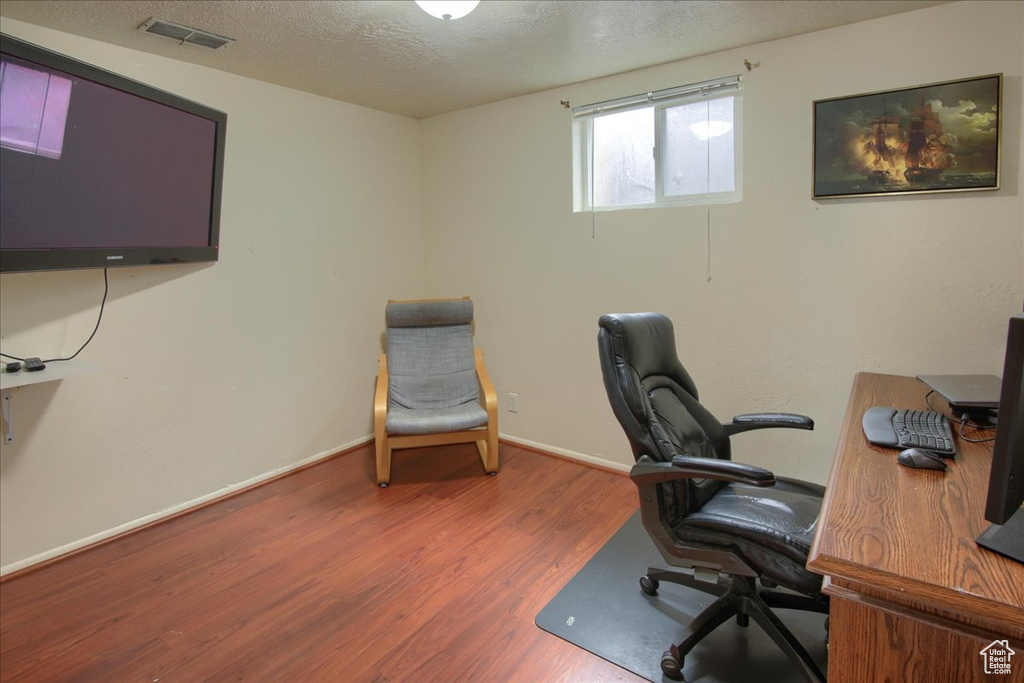 Office featuring baseboards, visible vents, wood finished floors, and a textured ceiling