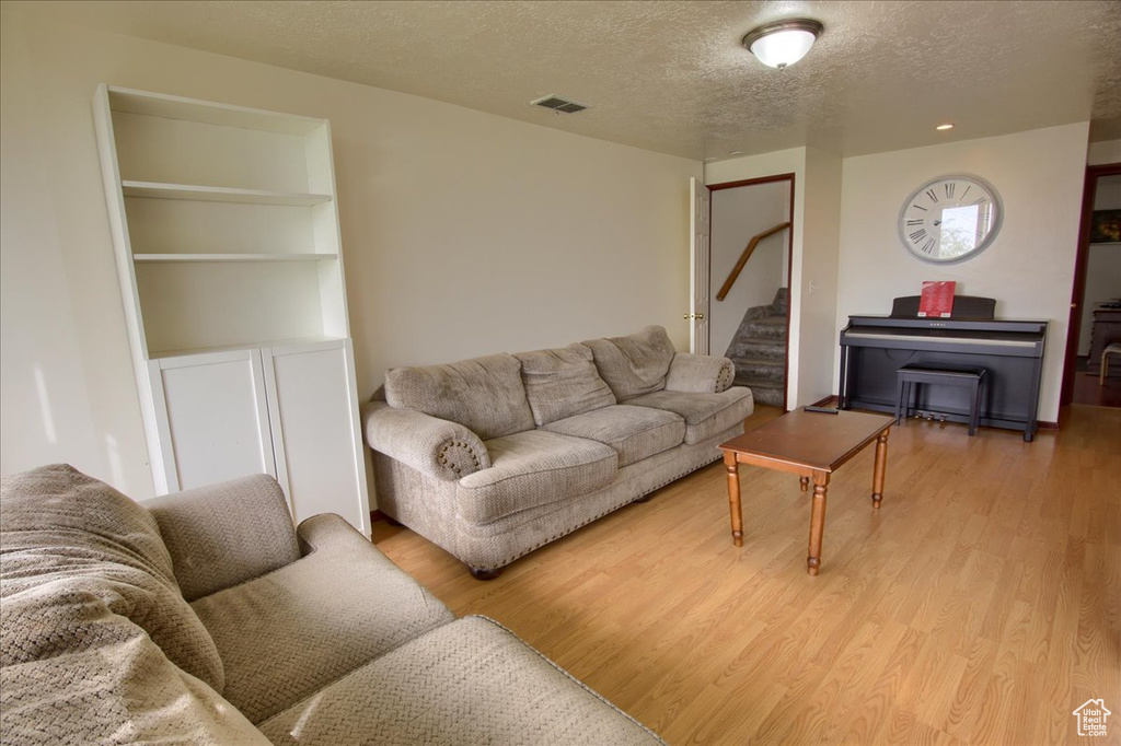 Living room with stairway, a textured ceiling, visible vents, and light wood-type flooring