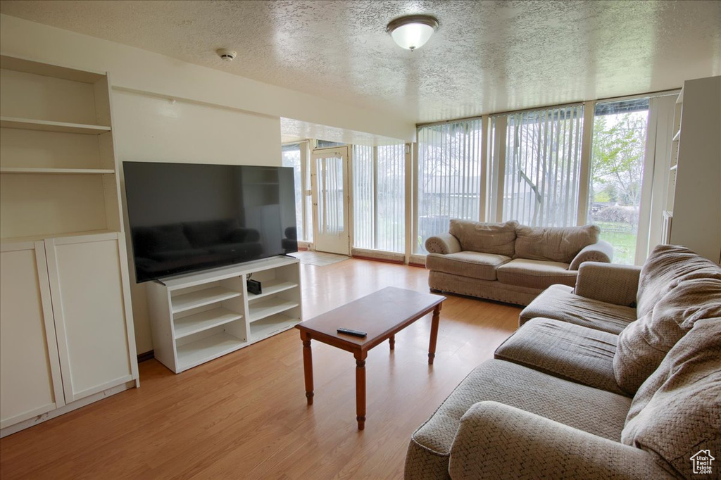 Living area with a wealth of natural light, light wood-style floors, a textured ceiling, and floor to ceiling windows