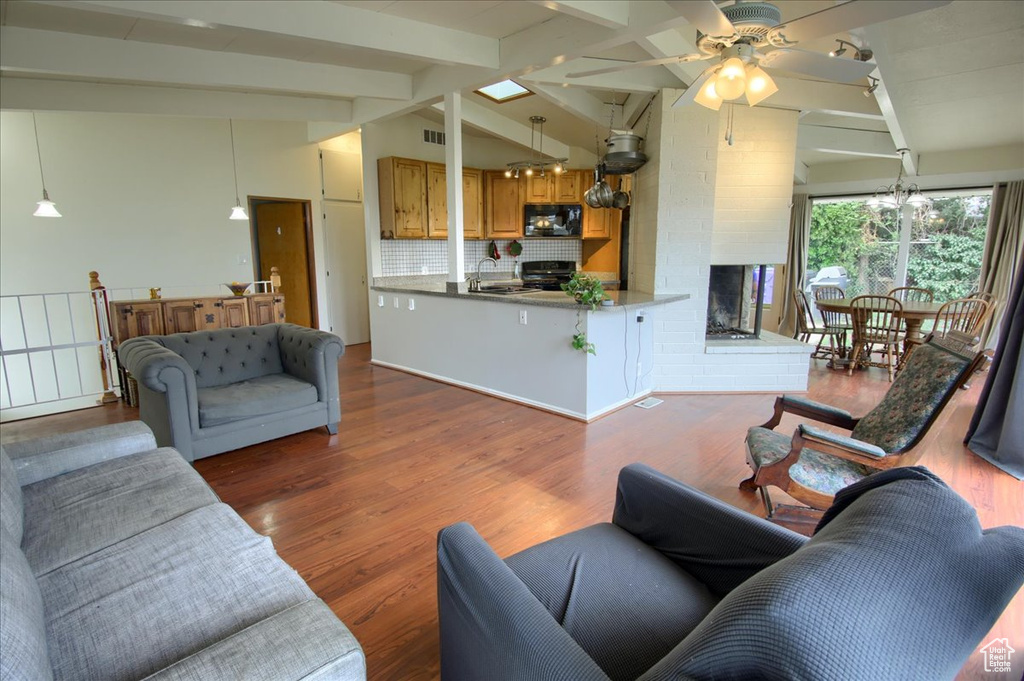 Living room featuring a ceiling fan, wood finished floors, and vaulted ceiling with beams