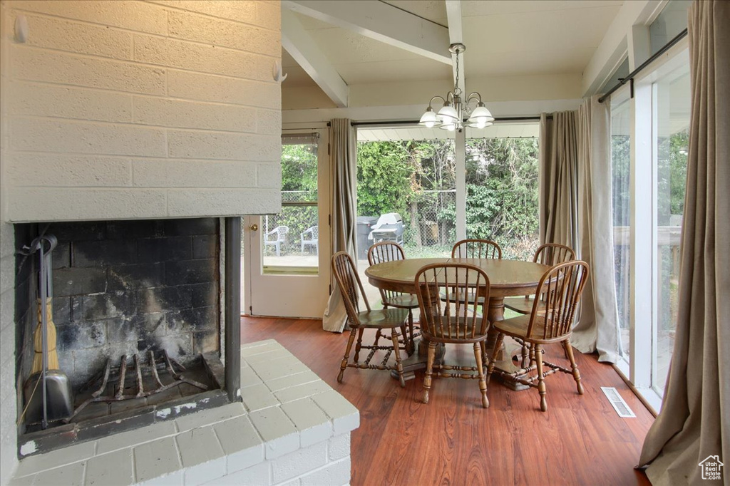 Dining room with beam ceiling, visible vents, a chandelier, wood finished floors, and a fireplace