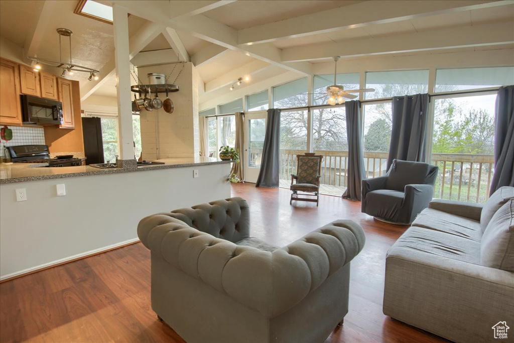 Living area with a healthy amount of sunlight, vaulted ceiling with beams, and dark wood-type flooring