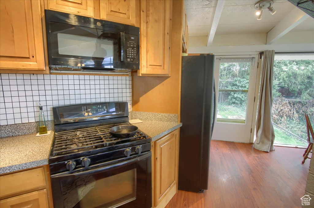 Kitchen featuring wood finished floors, beam ceiling, black appliances, and tasteful backsplash