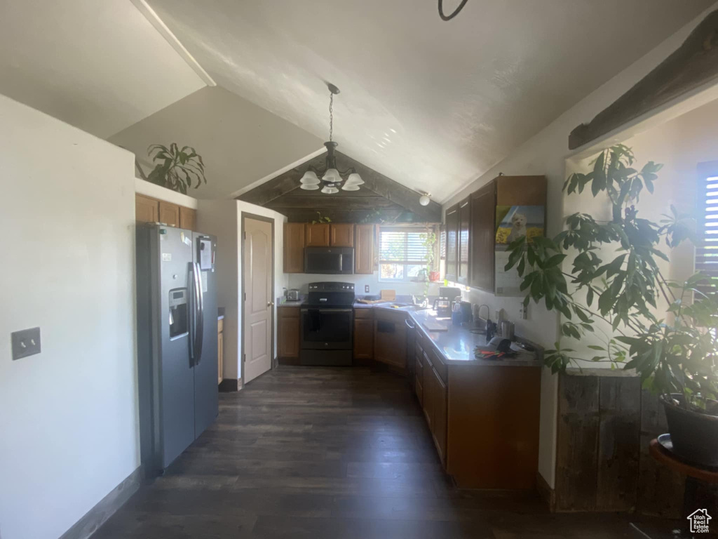 Kitchen featuring appliances with stainless steel finishes, vaulted ceiling, dark wood-type flooring, brown cabinetry, and pendant lighting