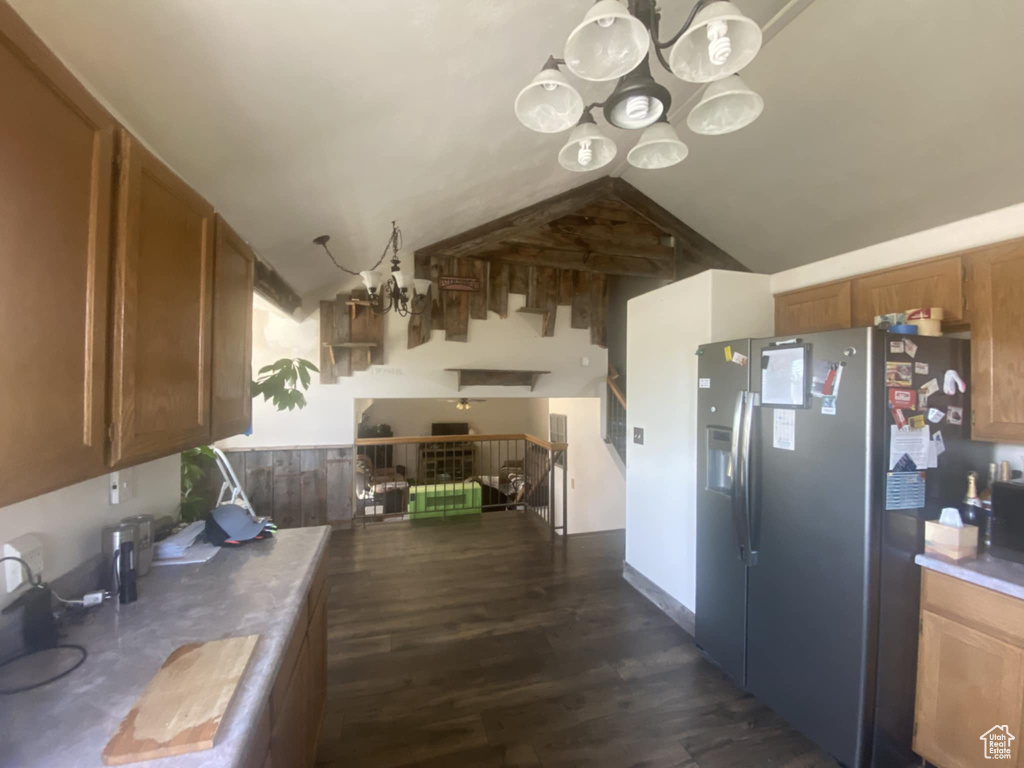 Kitchen with a chandelier, stainless steel refrigerator with ice dispenser, dark wood-style flooring, brown cabinetry, and vaulted ceiling